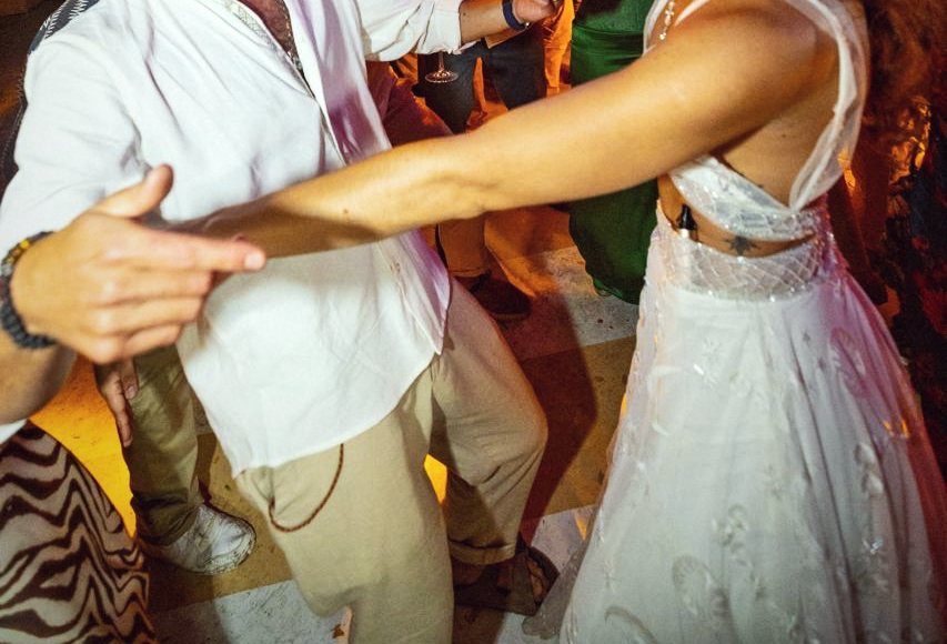 Detalle de una pareja bailando en la pista, vestido blanco y camisa de lino