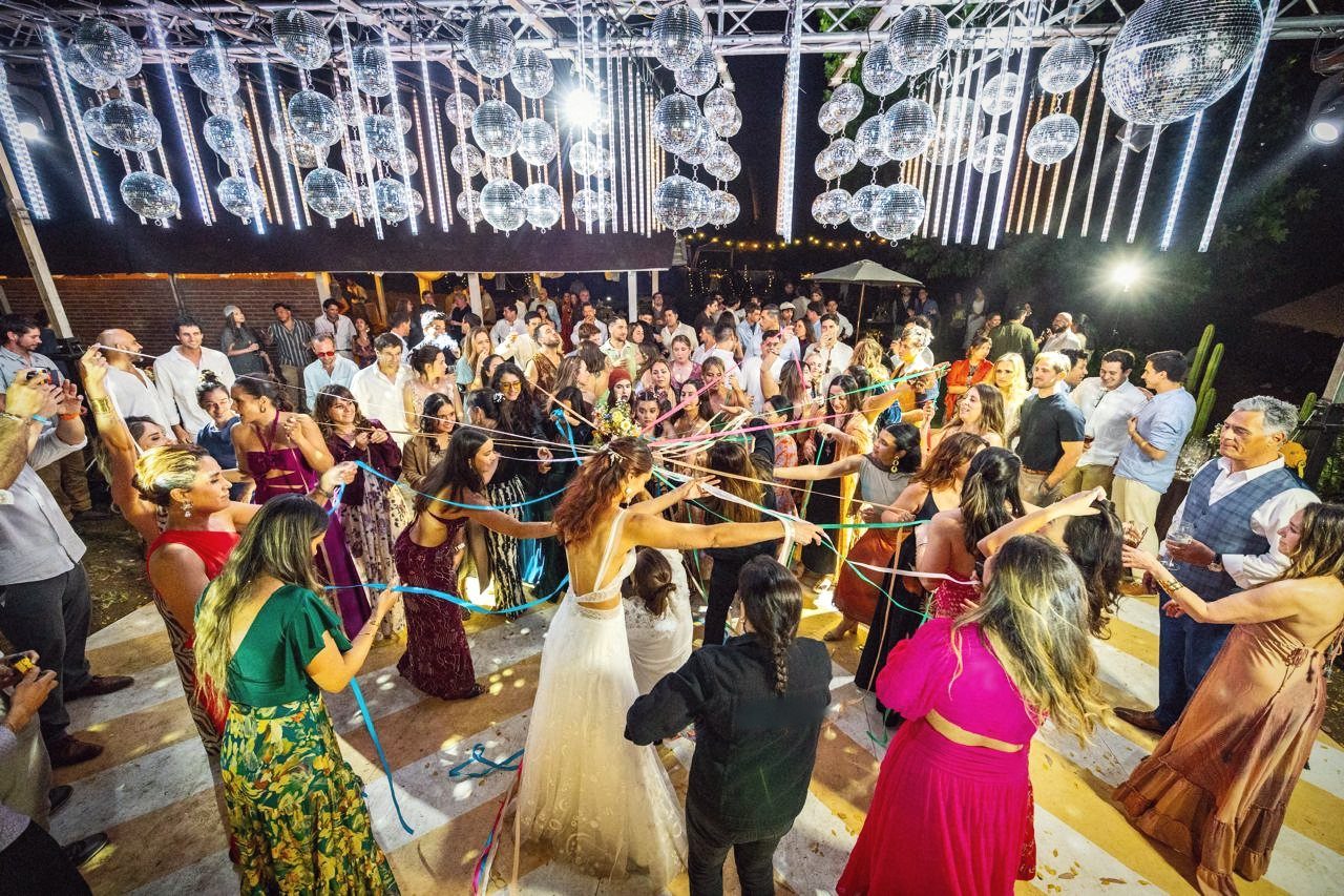 Baile de las cintas en la pista, con esferas espejadas y luces colgando sobre los invitados
